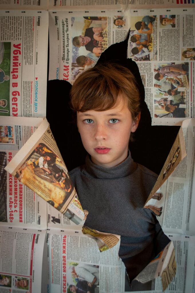 pexels-photo-9785207-9785207 Child breaking through torn newspapers, expressing curiosity and wonder.