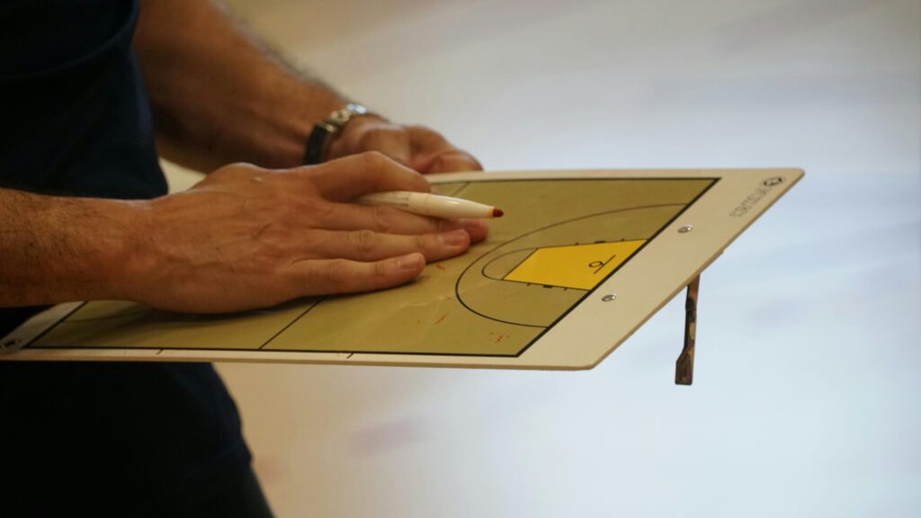 pexels-photo-32688082-32688082 Close-up of a coach using a basketball tactics board to plan game strategy indoors.